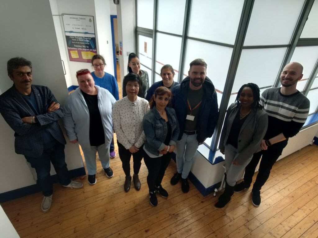 L to R: Ezzaldin, Mary, Marta, Eva, Csilla, Salwa, Maria, Marty, Nattassa, Dan, standing in the hallway of Accidental Theatre Belfast, all smiling widely