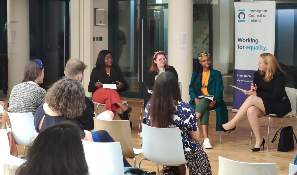 Lord Mayor Uruemu Adejinmi (in black and pink), Aga Wypychowska (red haired with headband), Joy Eniola (in yellow and Green, with multicoloured headband) and Lucy Michael (in a black skirt suit), in front of a crowd at the Immigrant council of Ireland conference. 